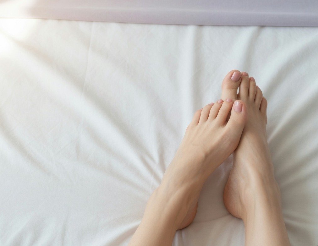 Bare feet resting on a light bedsheet, illustrating a typical non-explicit feet pic listing